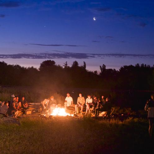 Unge som sidder udendørs om et bål i mørket 